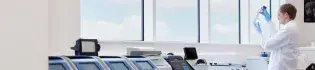 Scientist in lab standing infront of window, observing a vial