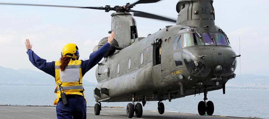 female Royal Navy sailor guides helicopter on aircraft carrier deck