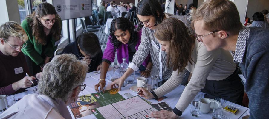 8 CRH researchers leaning over a table spread with news clippings and posters. They are in intense discussion