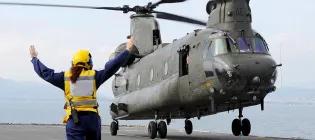 female Royal Navy sailor guides helicopter on aircraft carrier deck