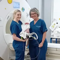 Two clinicians smiling with baby infront of MRI machine