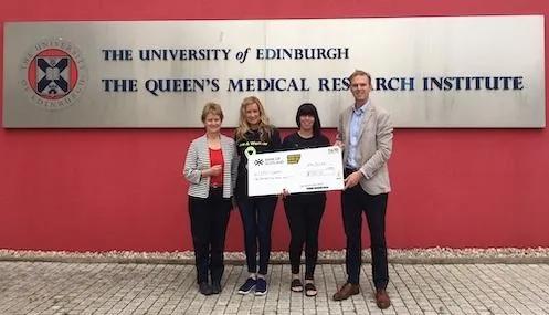 Support from Endo Warriors - people standing holding a giant cheque infront of The University of Edinbrugh, Queen's Medical Research Institute