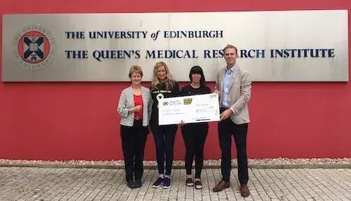 Support from Endo Warriors - people standing holding a giant cheque infront of The University of Edinbrugh, Queen's Medical Research Institute